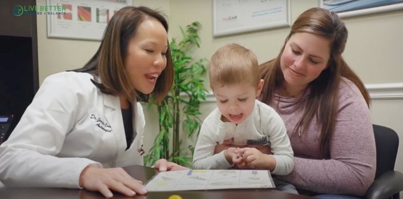 Dr. Cushing smiling as she goes over a picture card with a toddler sitting on his mother's lap