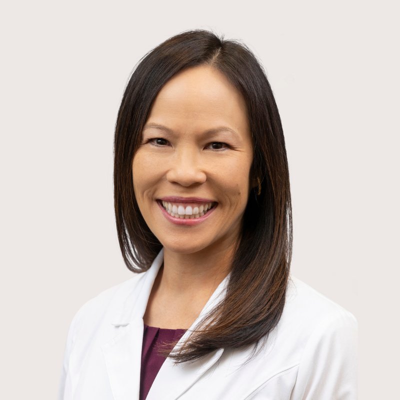 Dr. Jenifer Cushing, audiologist, smiling in a white coat over a plum top